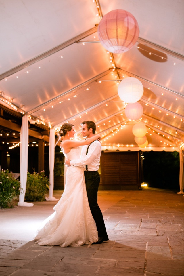 bride and groom stand under a lantern filled tent of sparkling lights at night