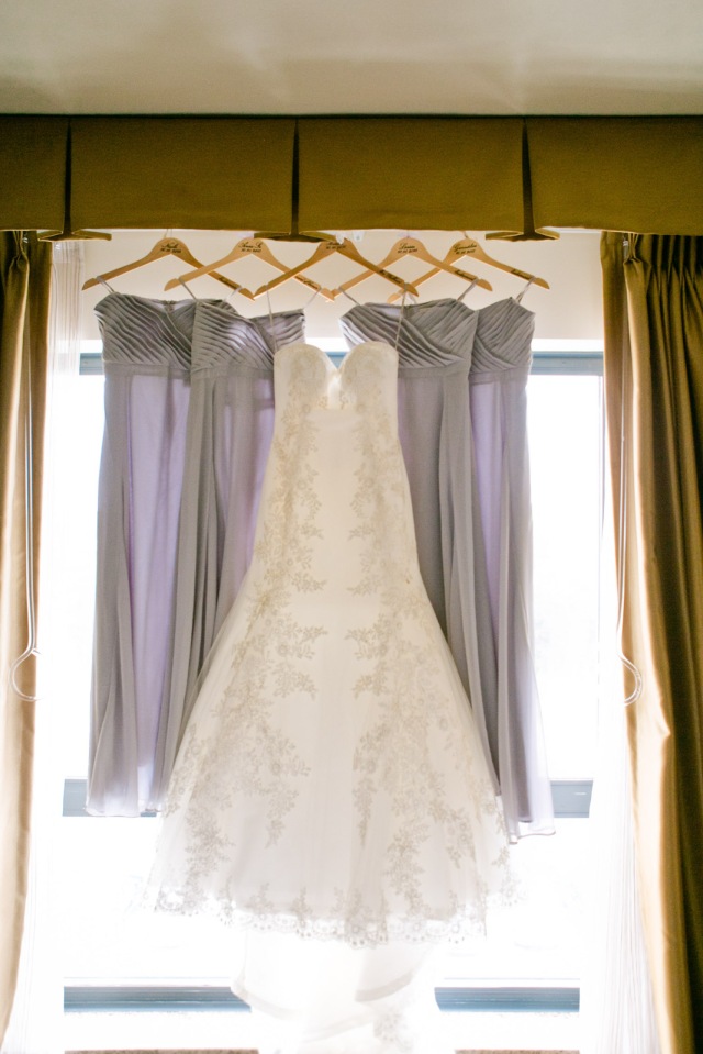 a brideswedding gown and lavender bridesmaid dresses hang in the light of a window