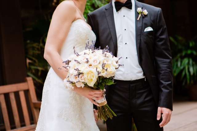 a bride and groom hold a ivory and purple bridal bouquet