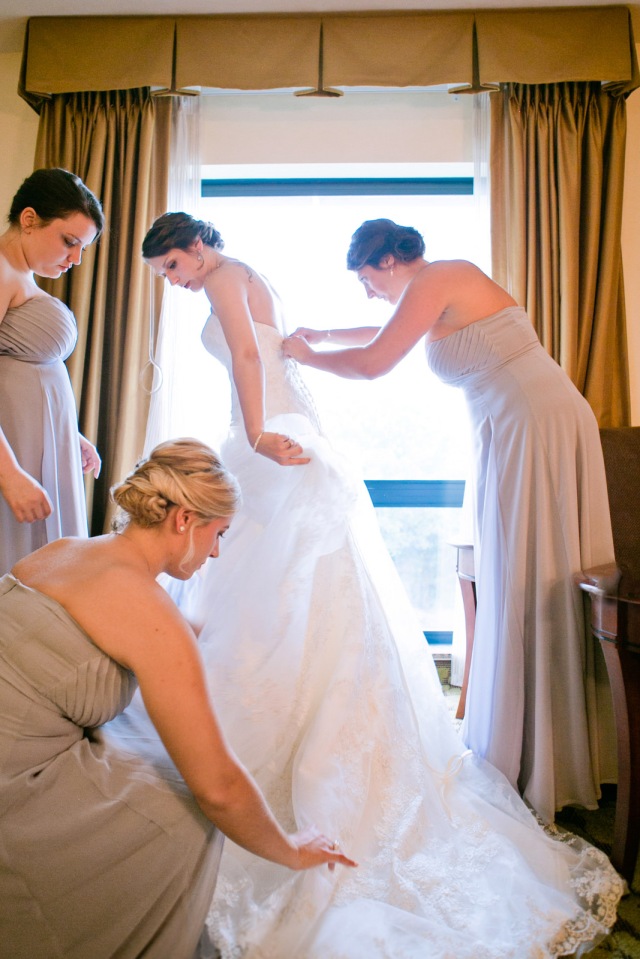 the bridesmaids surround the bride to assist her with her wedding dress before the wedding